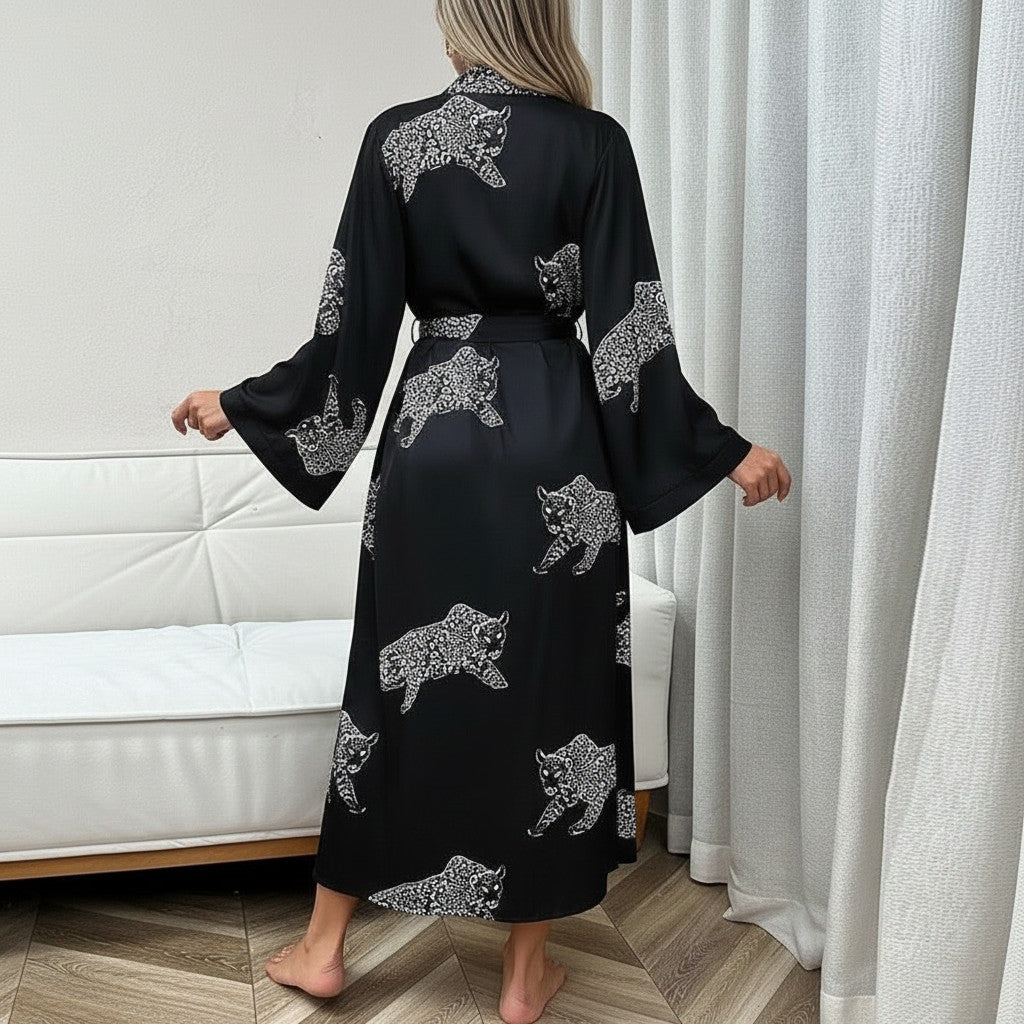 Mujer de espaldas vistiendo bata larga de satén negro vestismuse con estampado de leopardo blanco y mangas fluidas