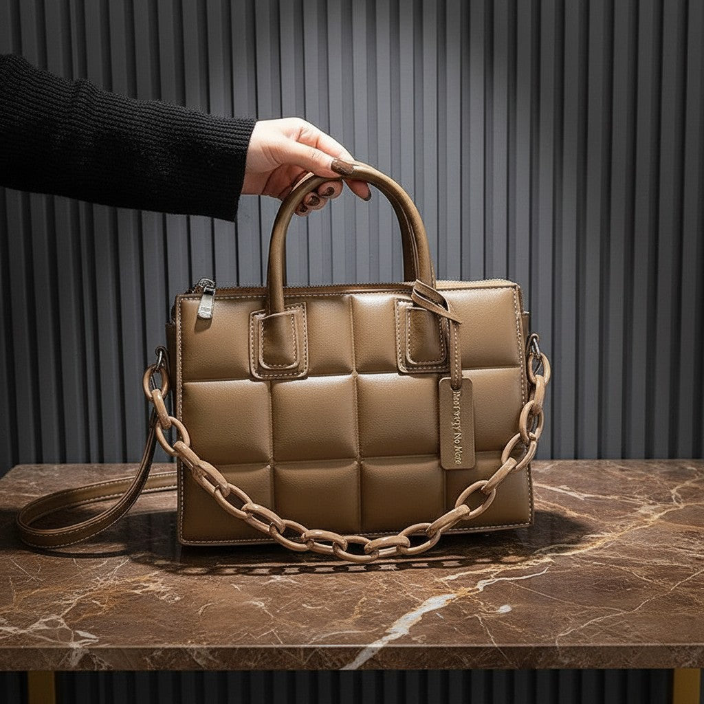 Bolso acolchado vestismuse color marrón con textura geométrica, asas cortas y detalle de cadena decorativa