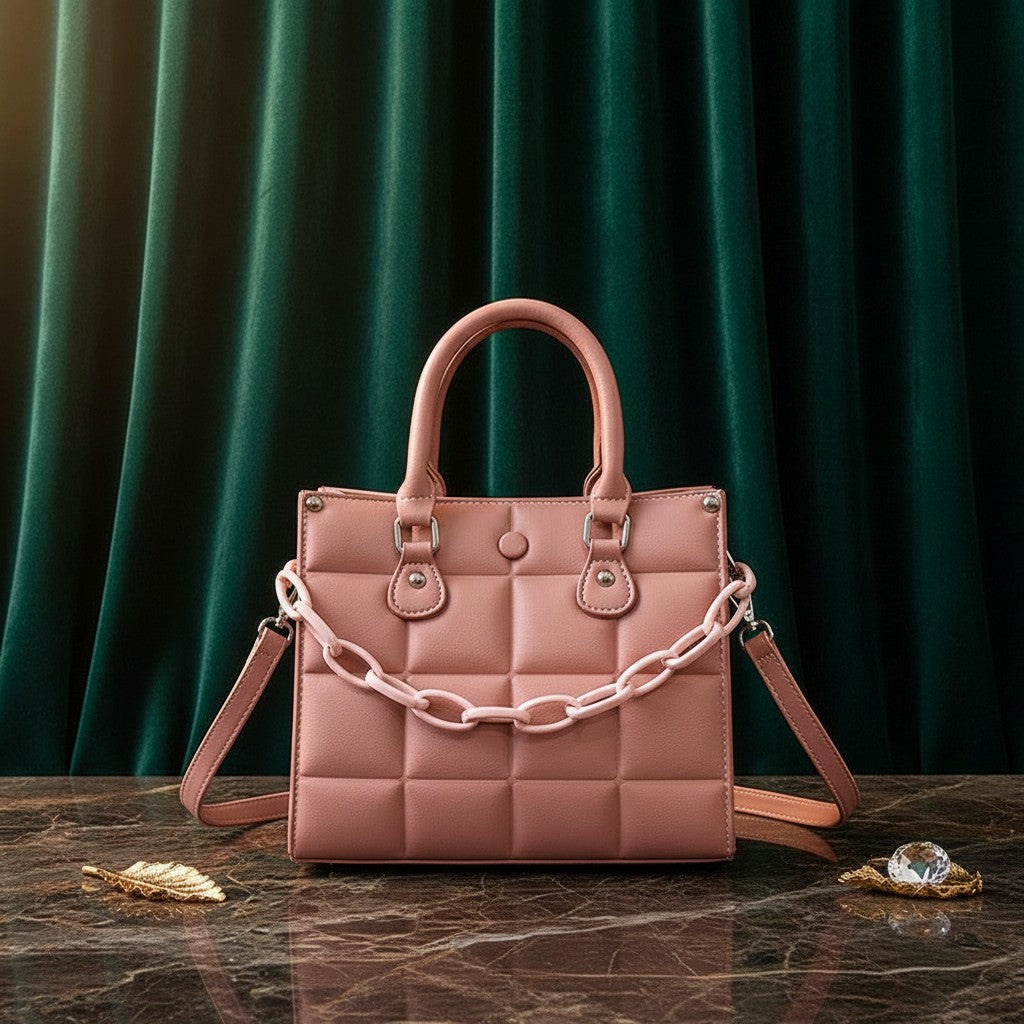 Bolso acolchado rosa vestismuse con cadena decorativa y asas cortas sobre mesa de mármol y fondo de cortina verde
