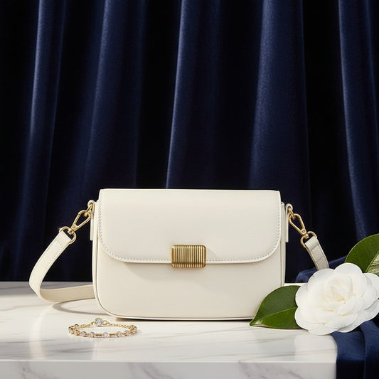 Bolso bandolera vestismuse blanco minimalista con solapa, cierre metálico y correa desmontable sobre mesa de mármol.