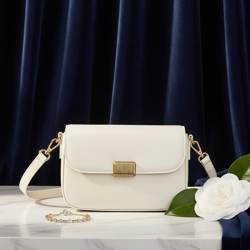 Bolso bandolera vestismuse blanco minimalista con solapa, cierre metálico y correa desmontable sobre mesa de mármol.